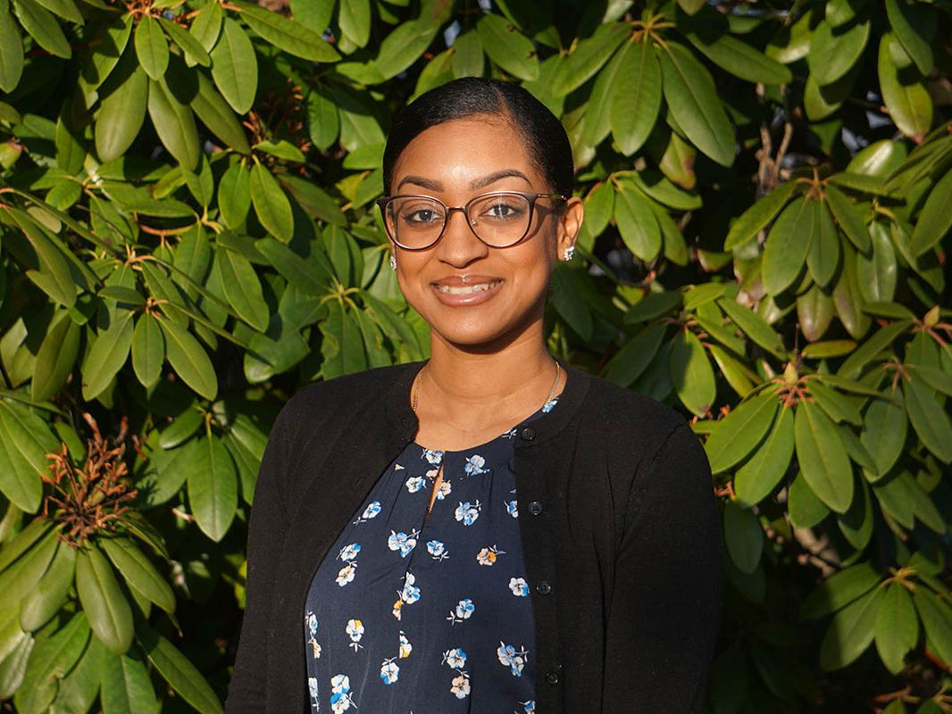 Woman smiling in front of green bushes.