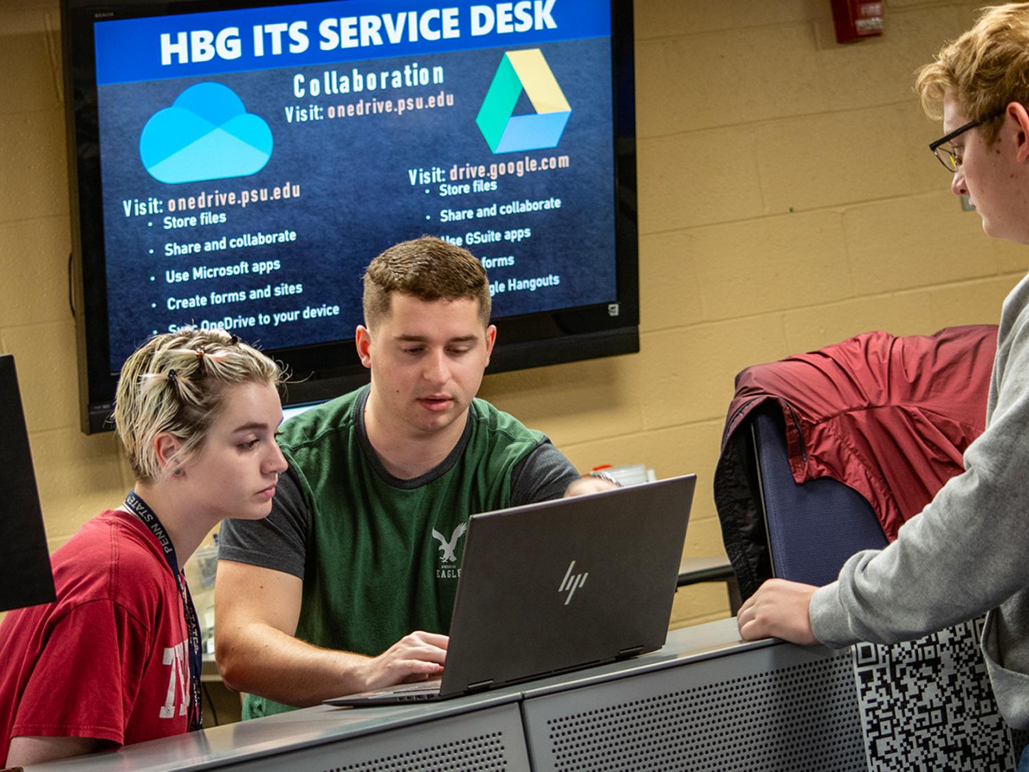 Student workers at the ITS Service desk look at someone's laptop.