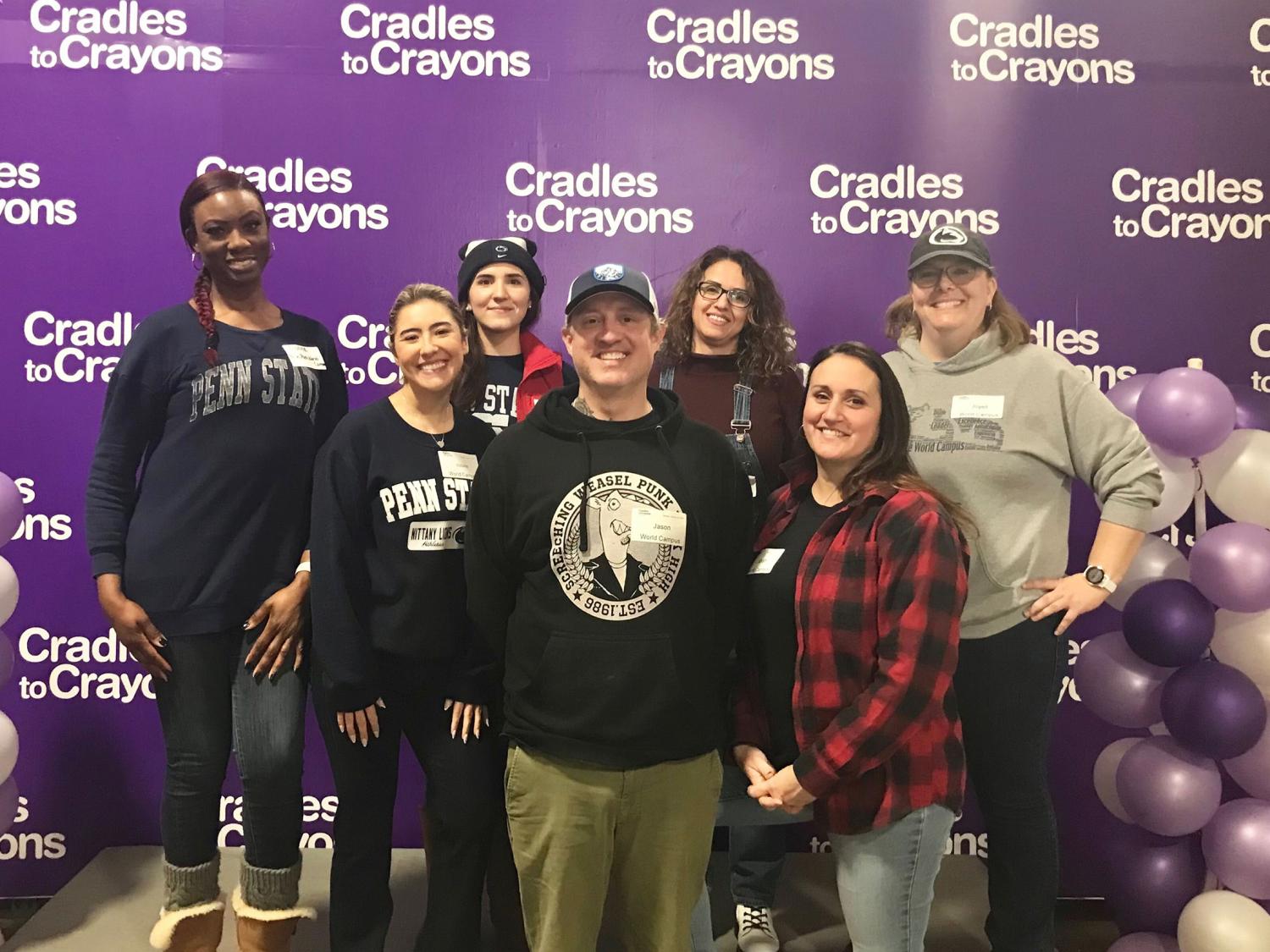 A group of seven people stand together in front of a purple backdrop.