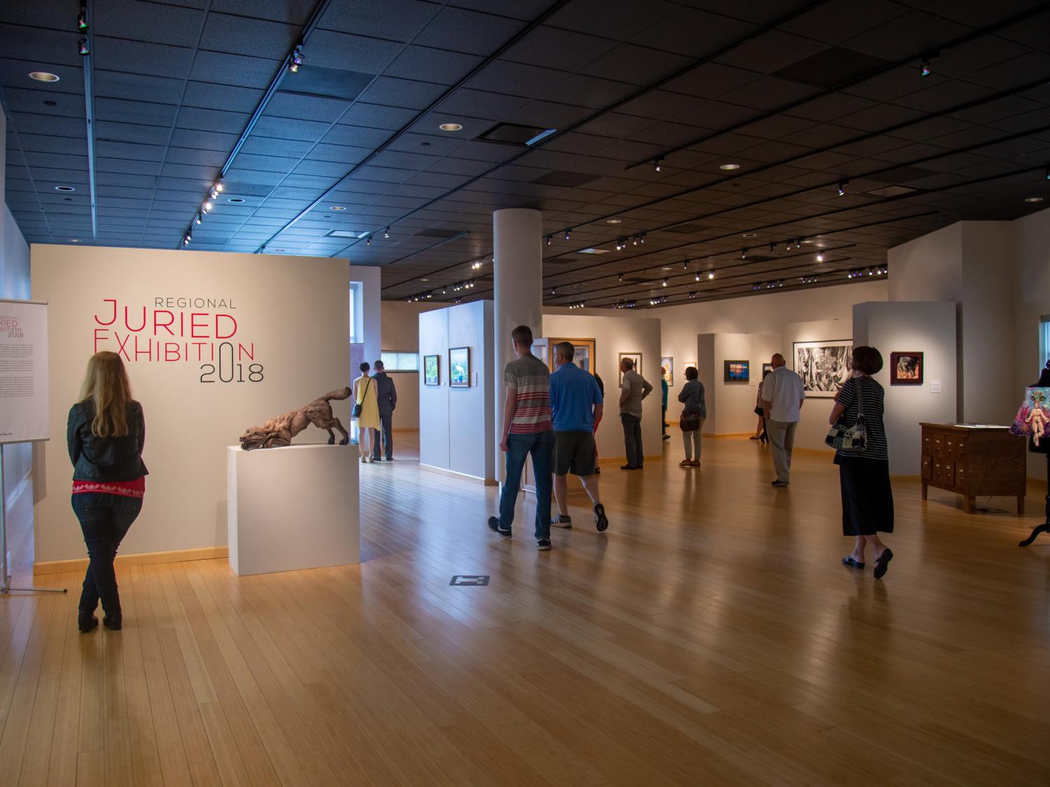 A wide view of an art gallery with wood floors and art on the walls.