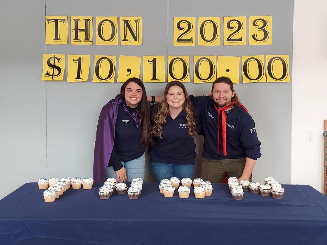 Three students stand smiling by table