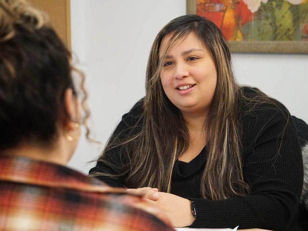 Woman seated at desk speaking with student seated across from her.