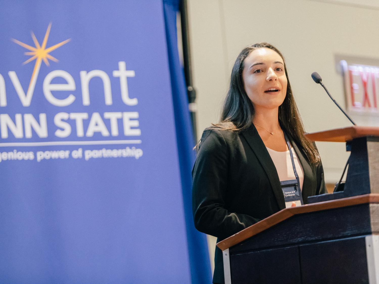 Marcella Marino stands behind a podium in front of an Invent Penn State sign pitching her startup idea.
