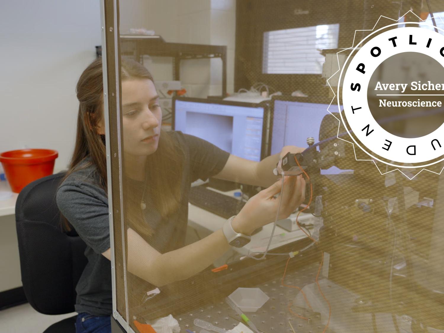 Avery Sicher seated at a lab bench, working with a scientific instrument