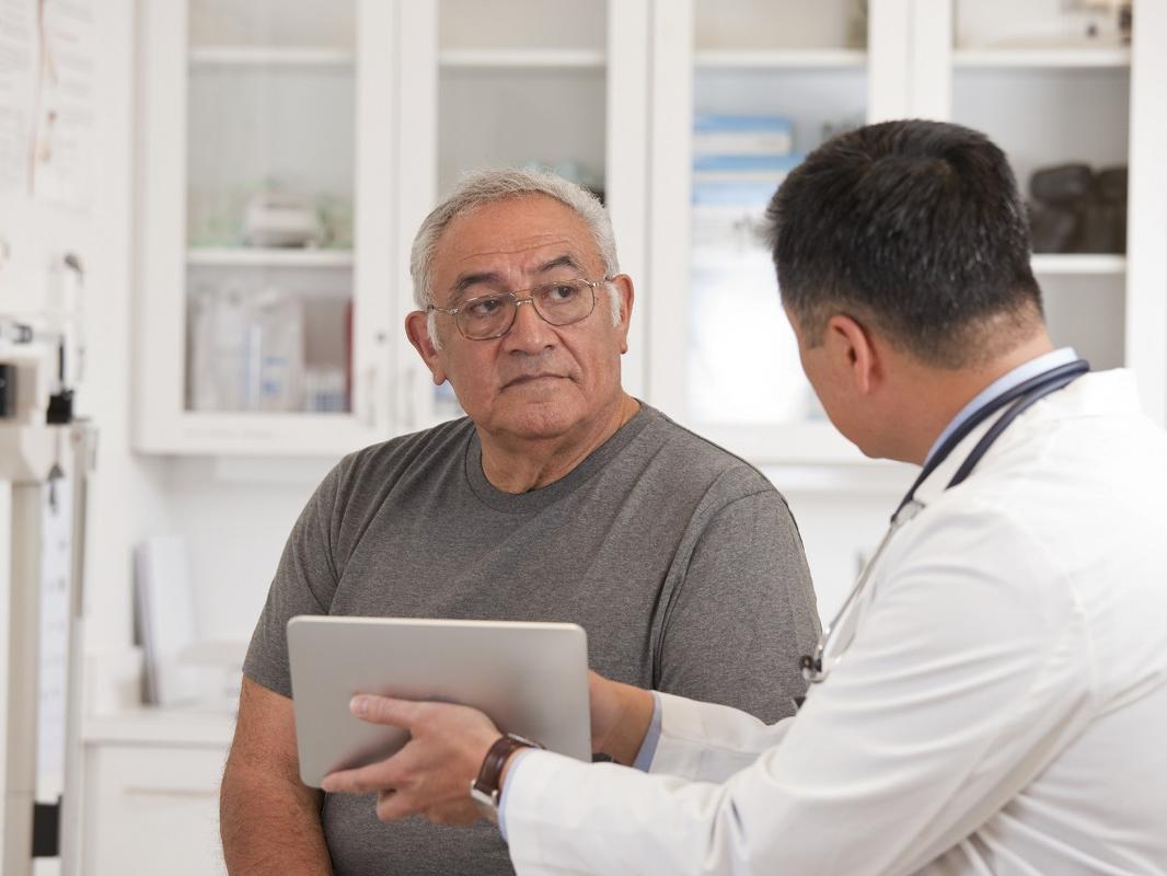 A doctor holds a digital tablet as he talks with a man.
