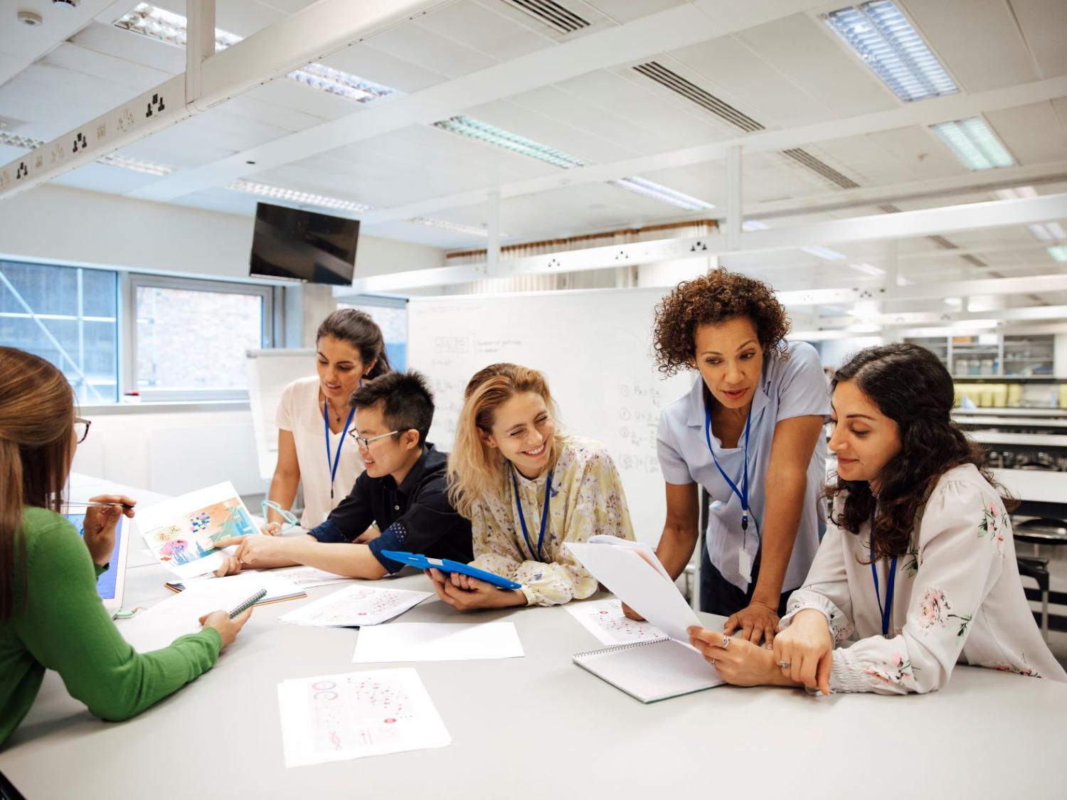 Adult students are gathered at a table working on an academic project together.