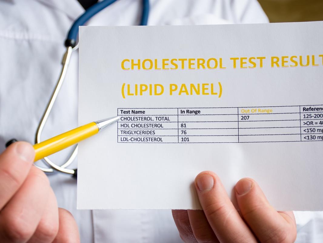 A physician uses a pen to point to a sheet of paper labeled “Cholesterol test result (Lipid panel).”