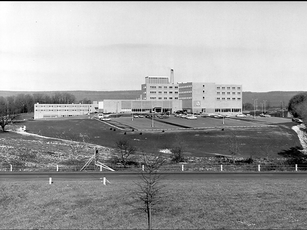 A black-and-white image of a hospital image with rolling hills in the background.