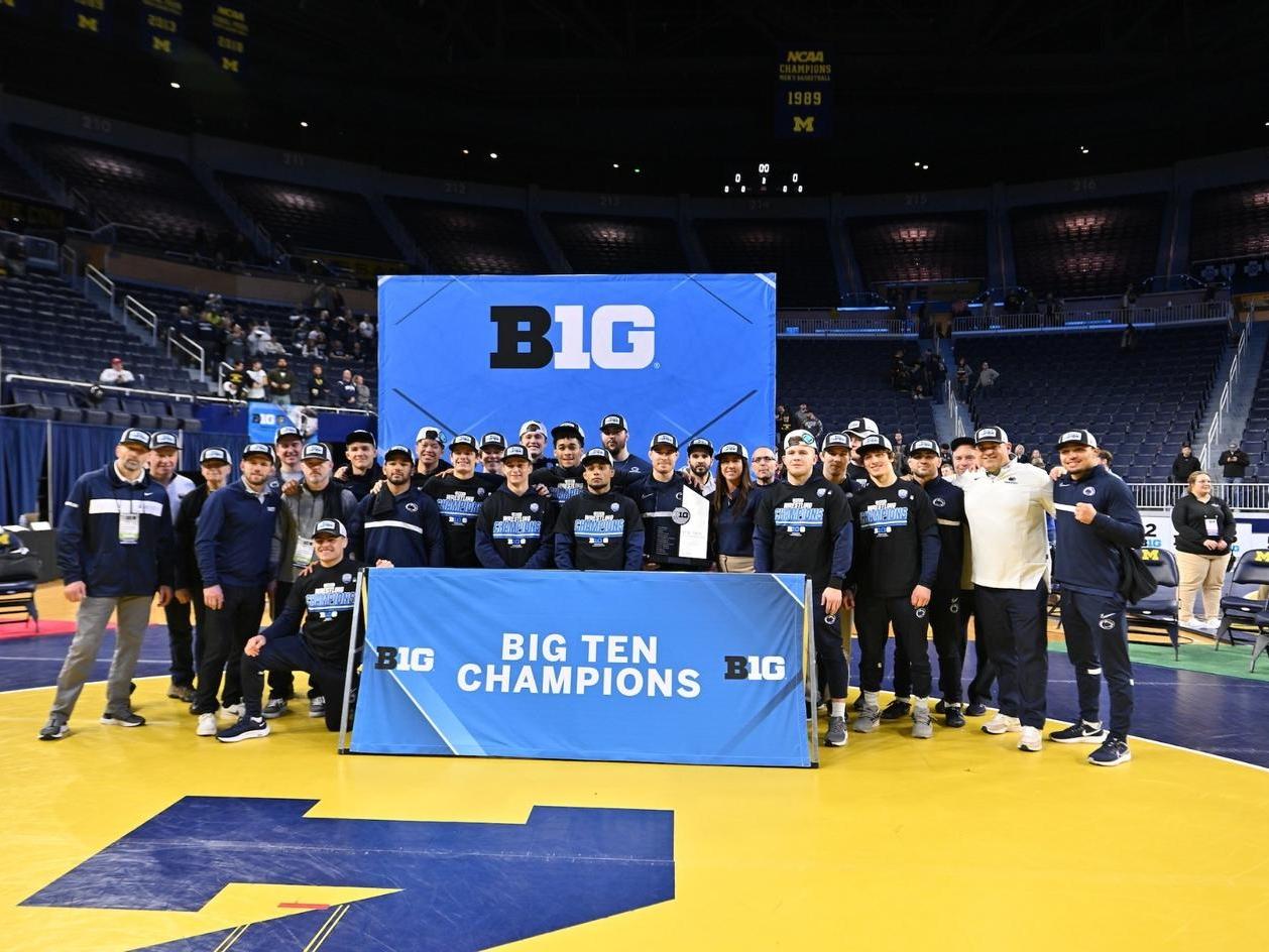 The Penn State wrestling team pose behind a sign that reads "Big Ten Champions"