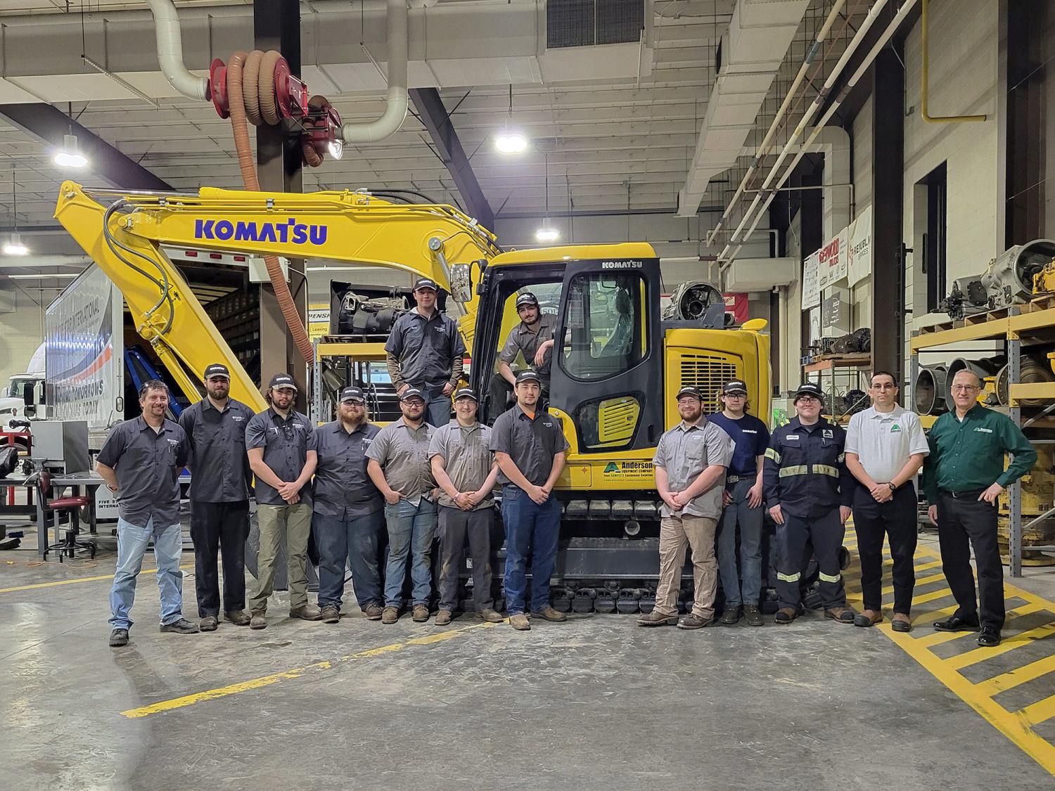Equipment representatives stand with Penn College students in front of excavator.