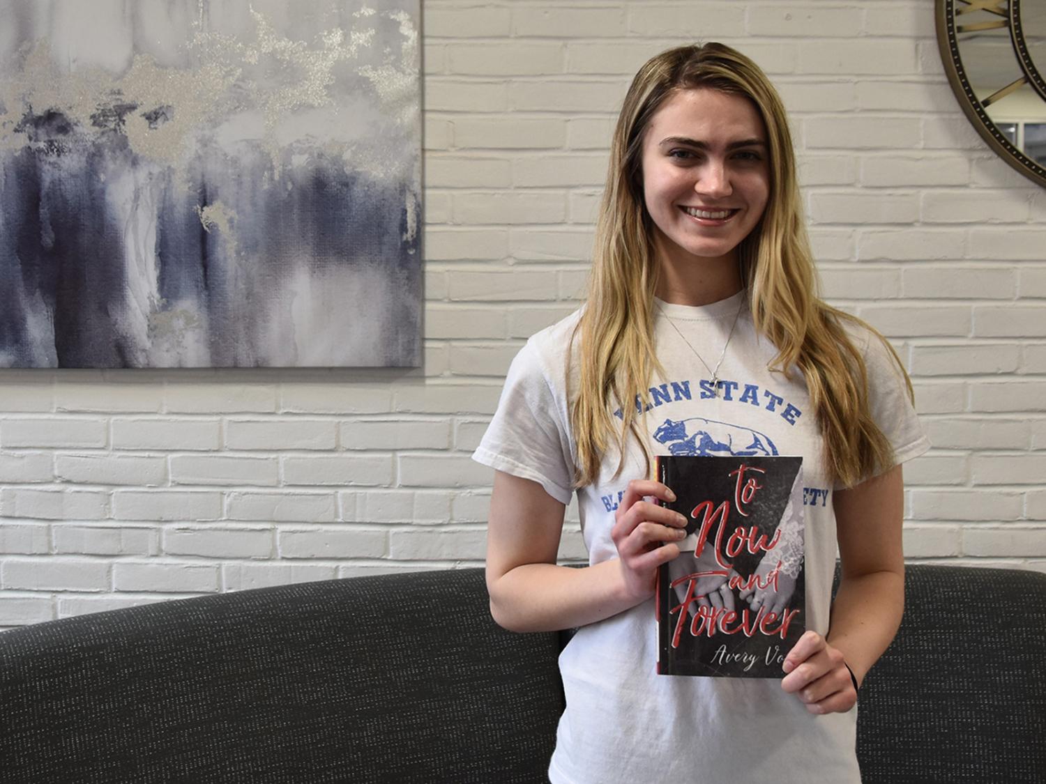 Young caucasian woman with long hair holding a book, art on the wall in the background.