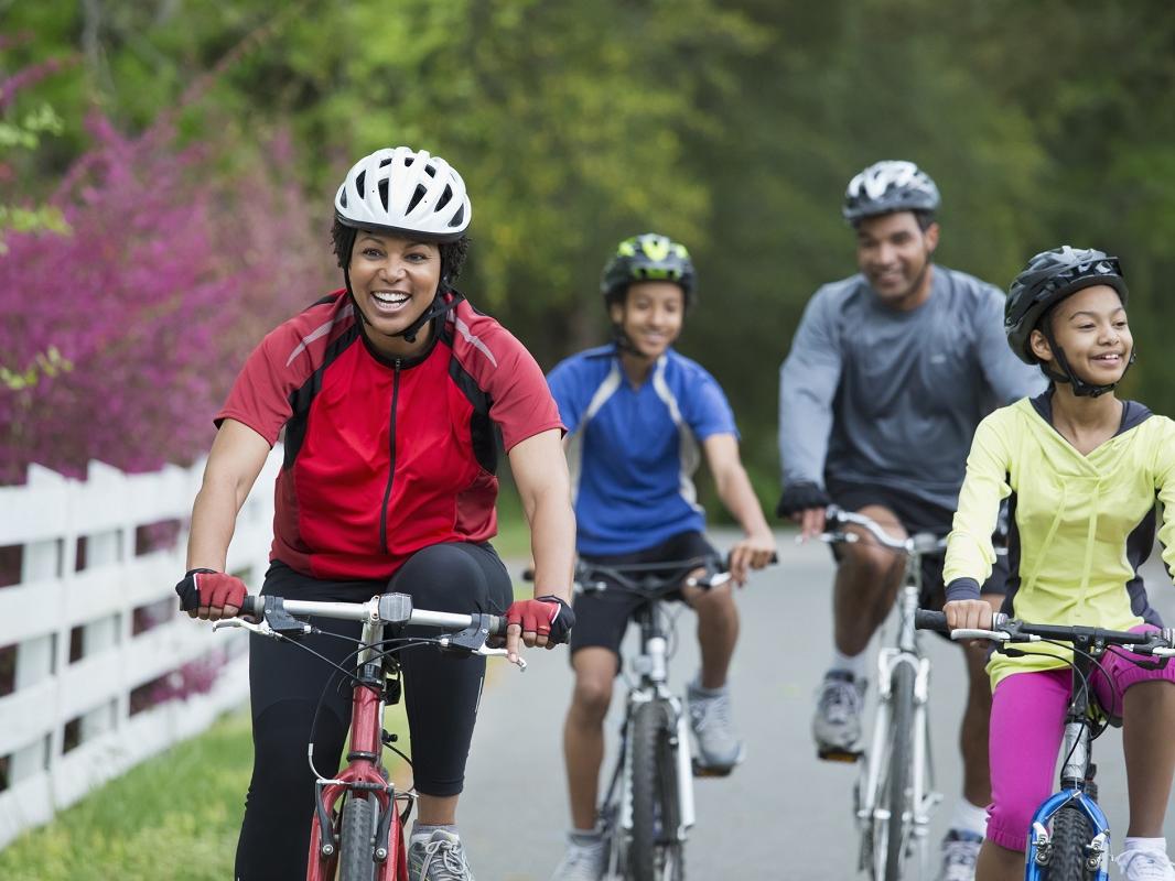A family of four rides bicycles together down a street.