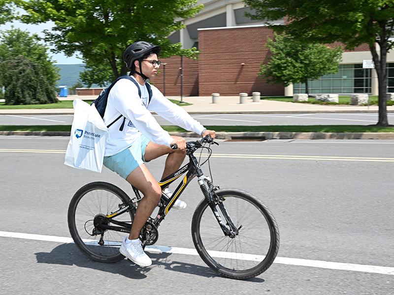 Student biking on the road past the Bryce Jordan Center.