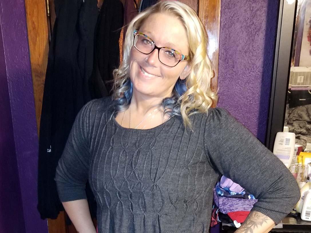 Woman with blonde hair and glasses in a gray dress.