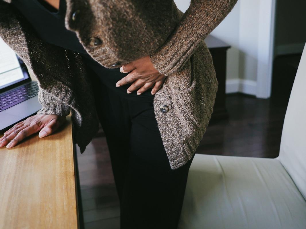 Close-up of a woman bending over a desk in pain.