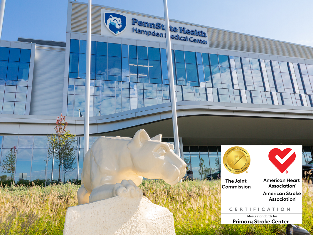 A statue of the Penn State Nittany lion sits next to the glass facade of Hampden Medical Center. Logos for the Joint Commission and the American Heart Association are superimposed.