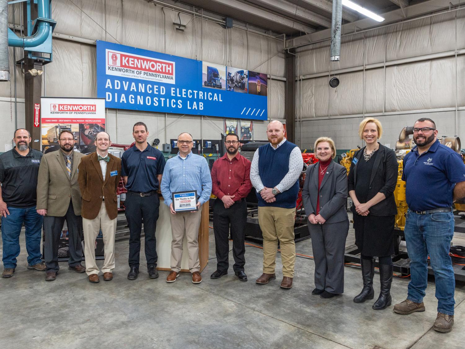 A group of people stand in a warehouse posing for a photograph with a big banner behind them