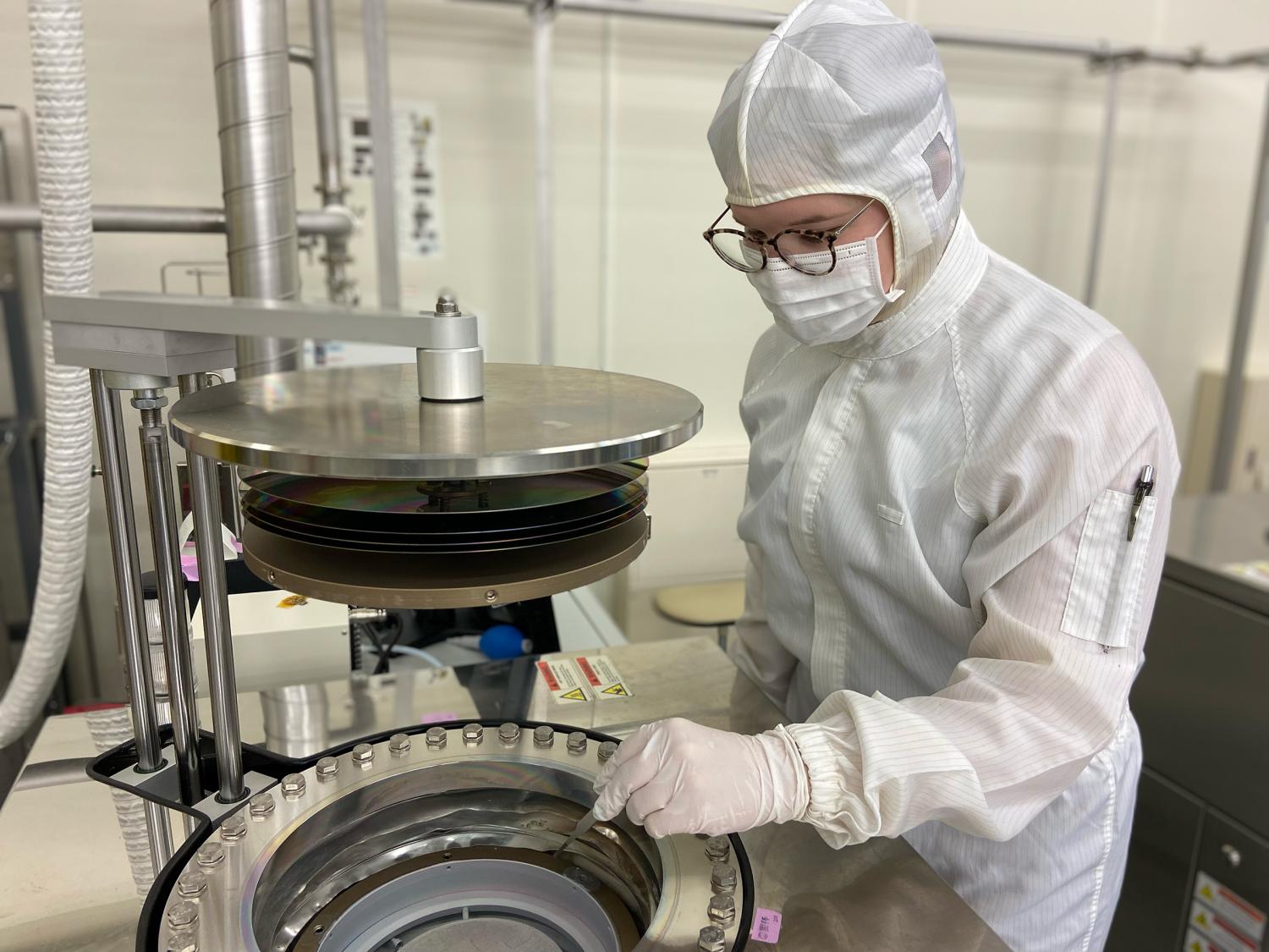 A researcher in a cleanroom standing next to a large metal instrument