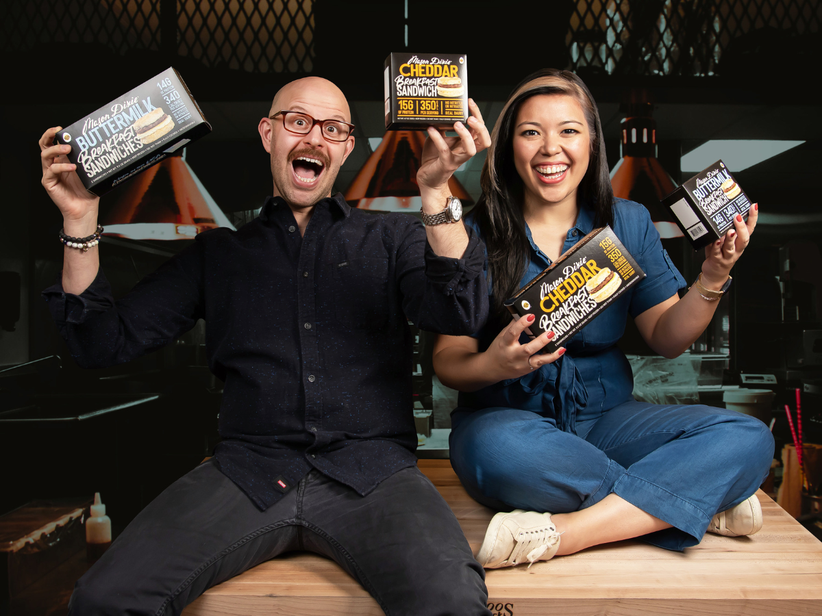 Ross Perkins and Ayeshah Abuelhiga sitting posing for a photo holding their frozen food products