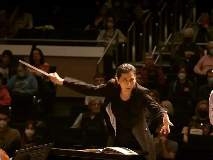 Woman with dark hair intensely conducting an orchestra