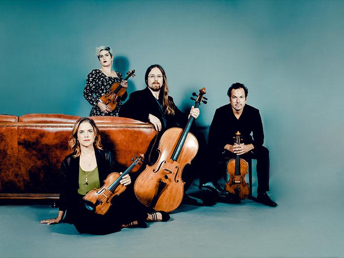 Four musicians holding string instruments on a brown leather couch
