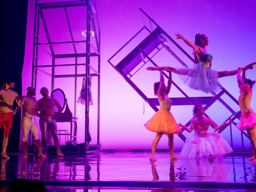 Three traditionally masculine-looking male athletes watch in awe as a group of four women perform feats of strength.