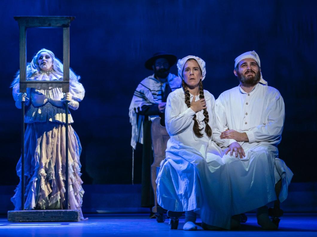 A ghostly figure hovers behind a middle-aged couple dressed in their nightclothes.