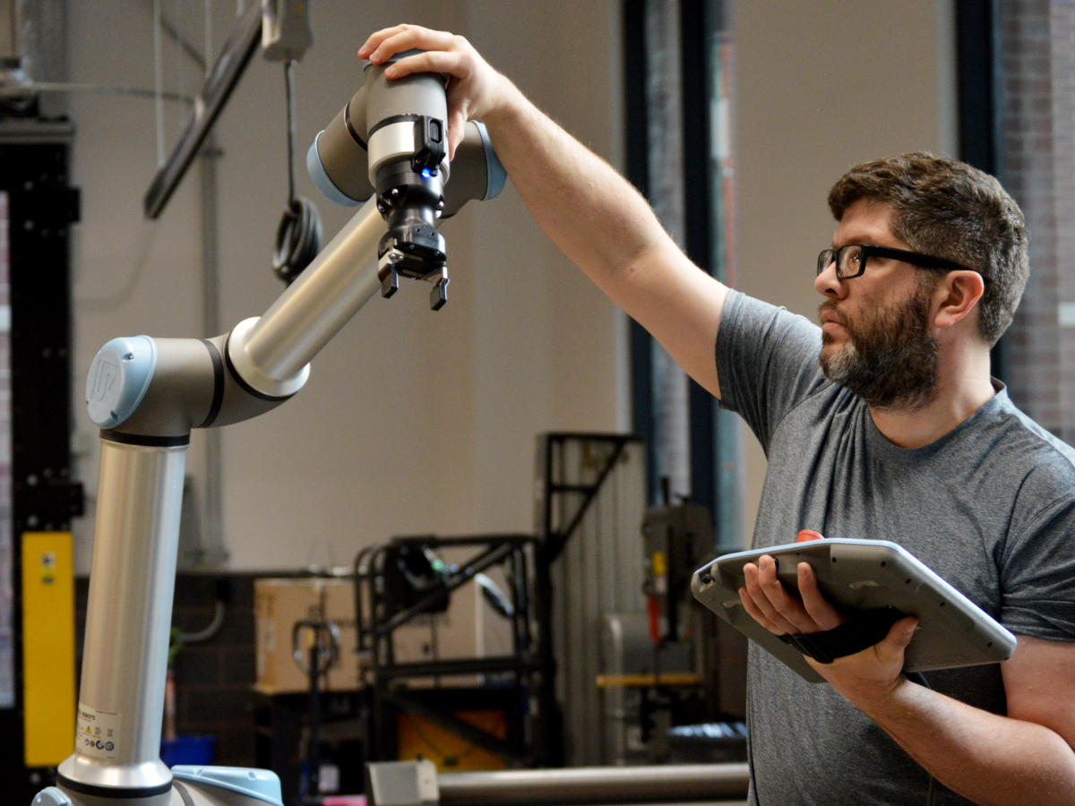 A man adjusts a robotic arm in the OriginLabs workshop
