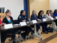 A panel of women sit behind a table in the Lodge on the campus of Penn State Beaver. There is a name card in front of each panelist.