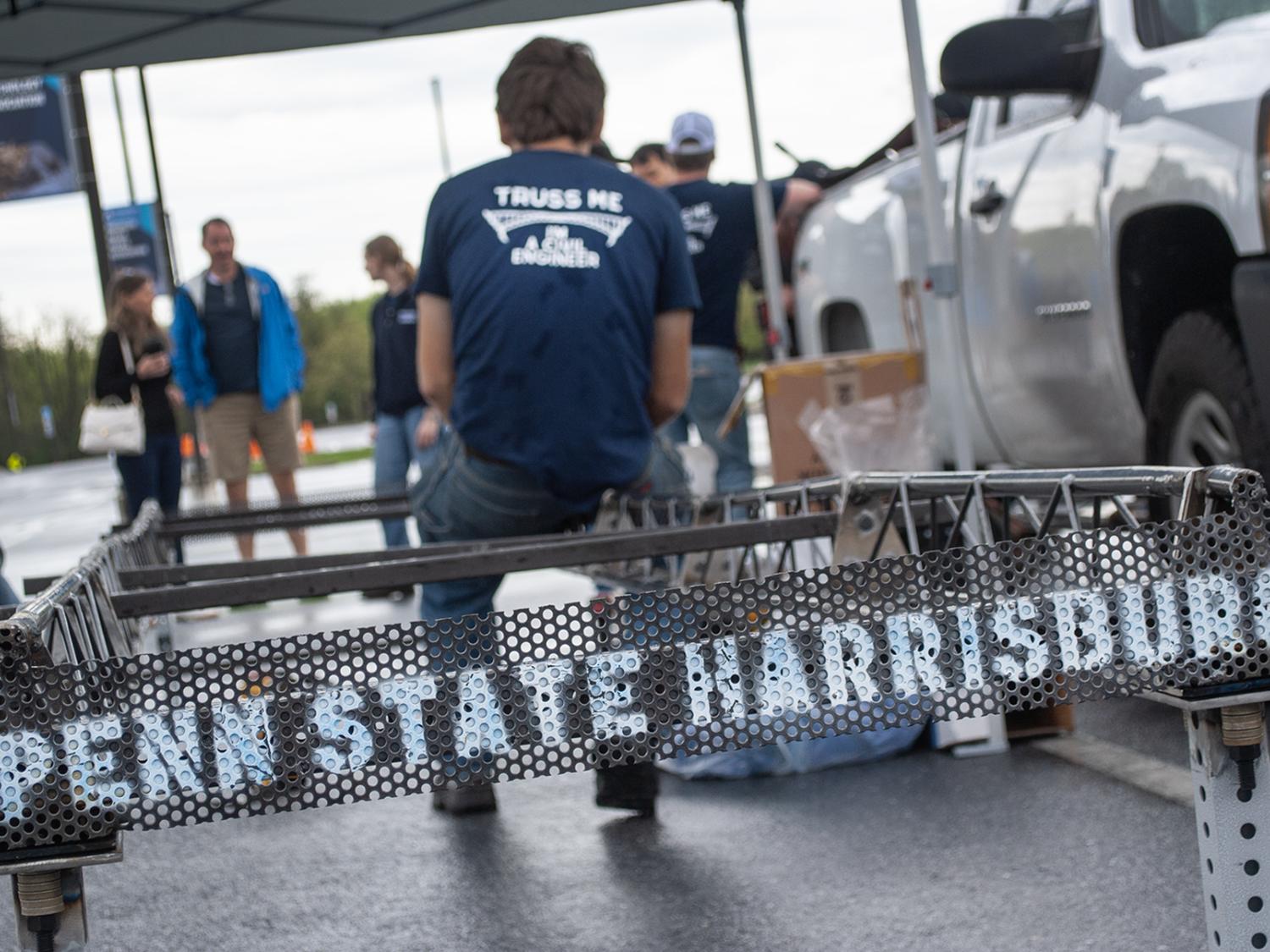 A student sits on the edge of a steel bridge that has "Penn State Harrisburg" painted on it