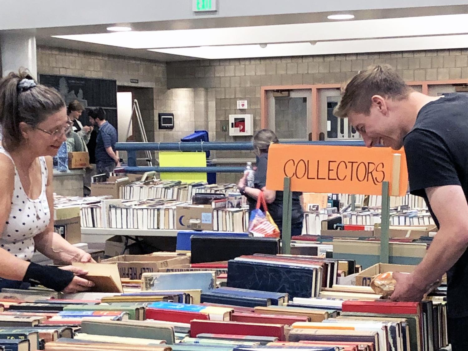 Two individuals comb through a table of books labeled "Collectors."