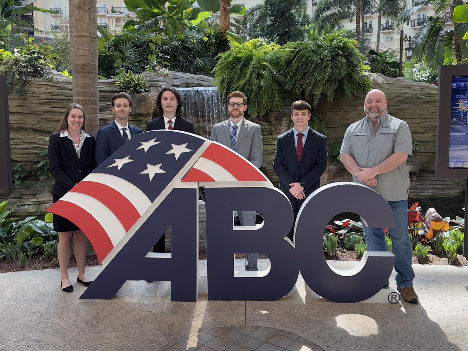 People stand behind a big ABC sign with an American flag. Palm trees are in the background.