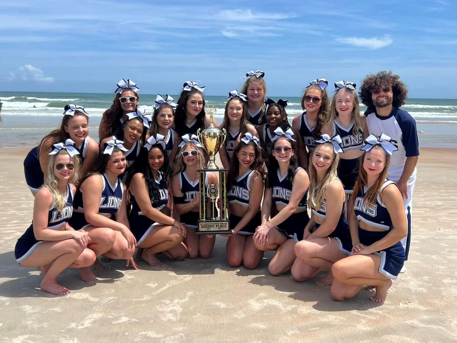 Penn State Behrend's competitive cheerleading team poses with a trophy on the beach in Florida.