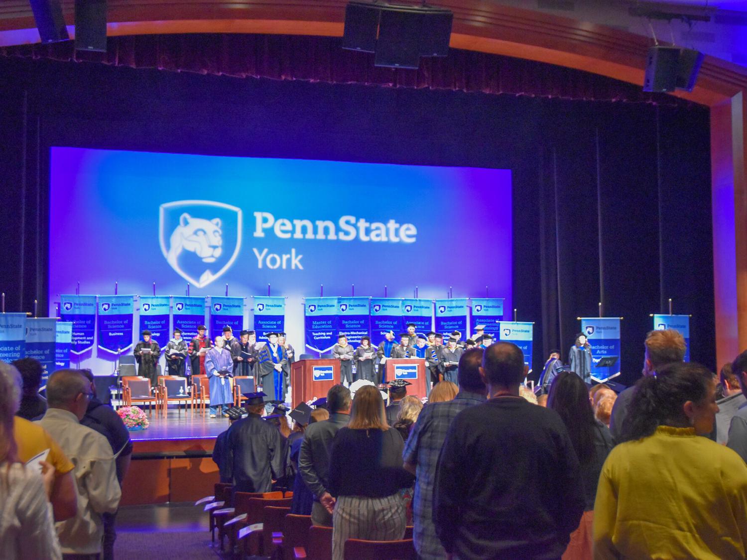 Theatre filled with people watch a commencement ceremony on stage