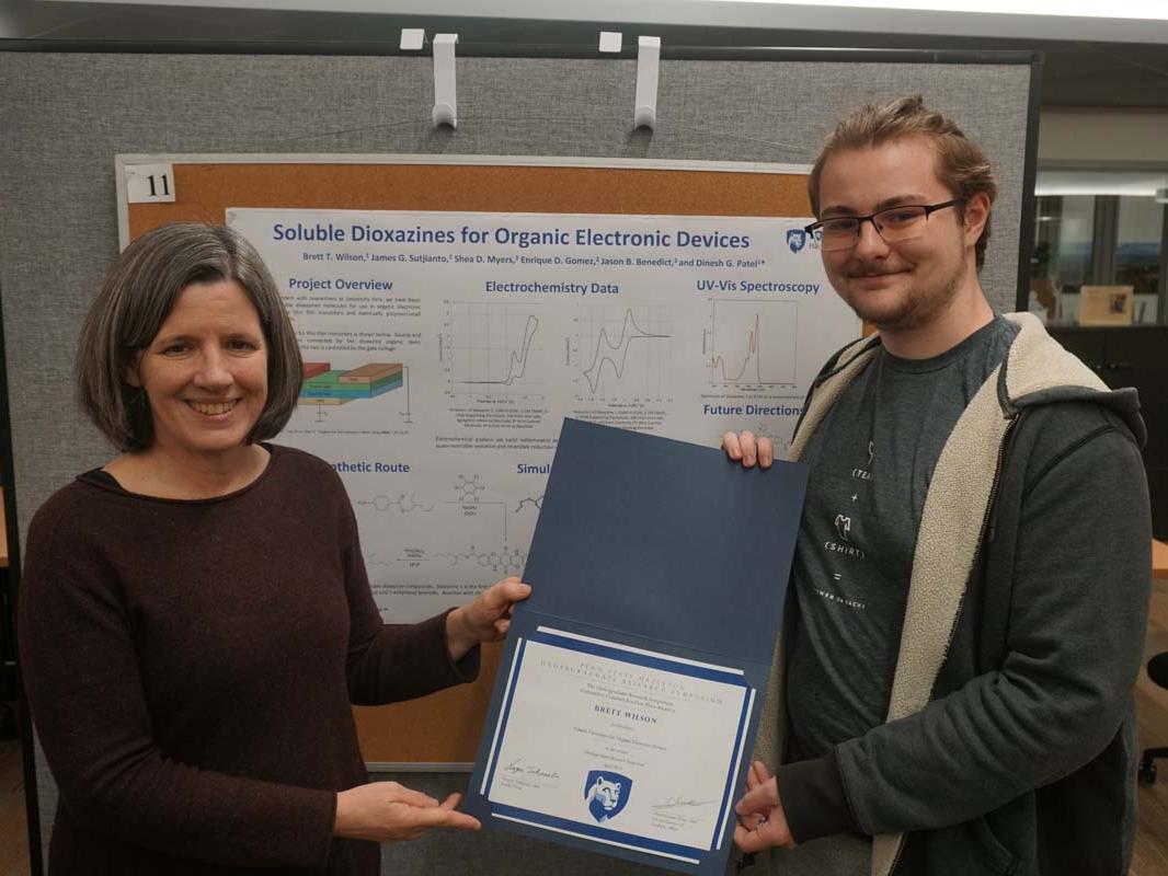Male student holding certificate next to female administrator.