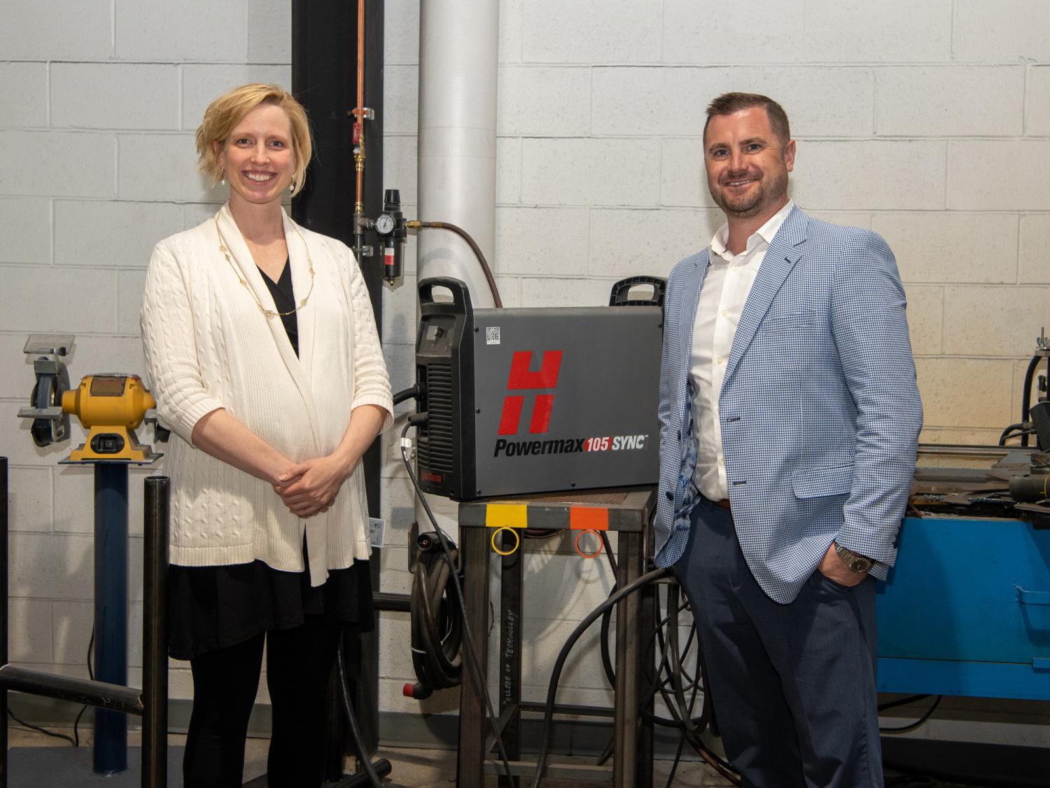 Two people in a welding lab stand next to a plasma system unit