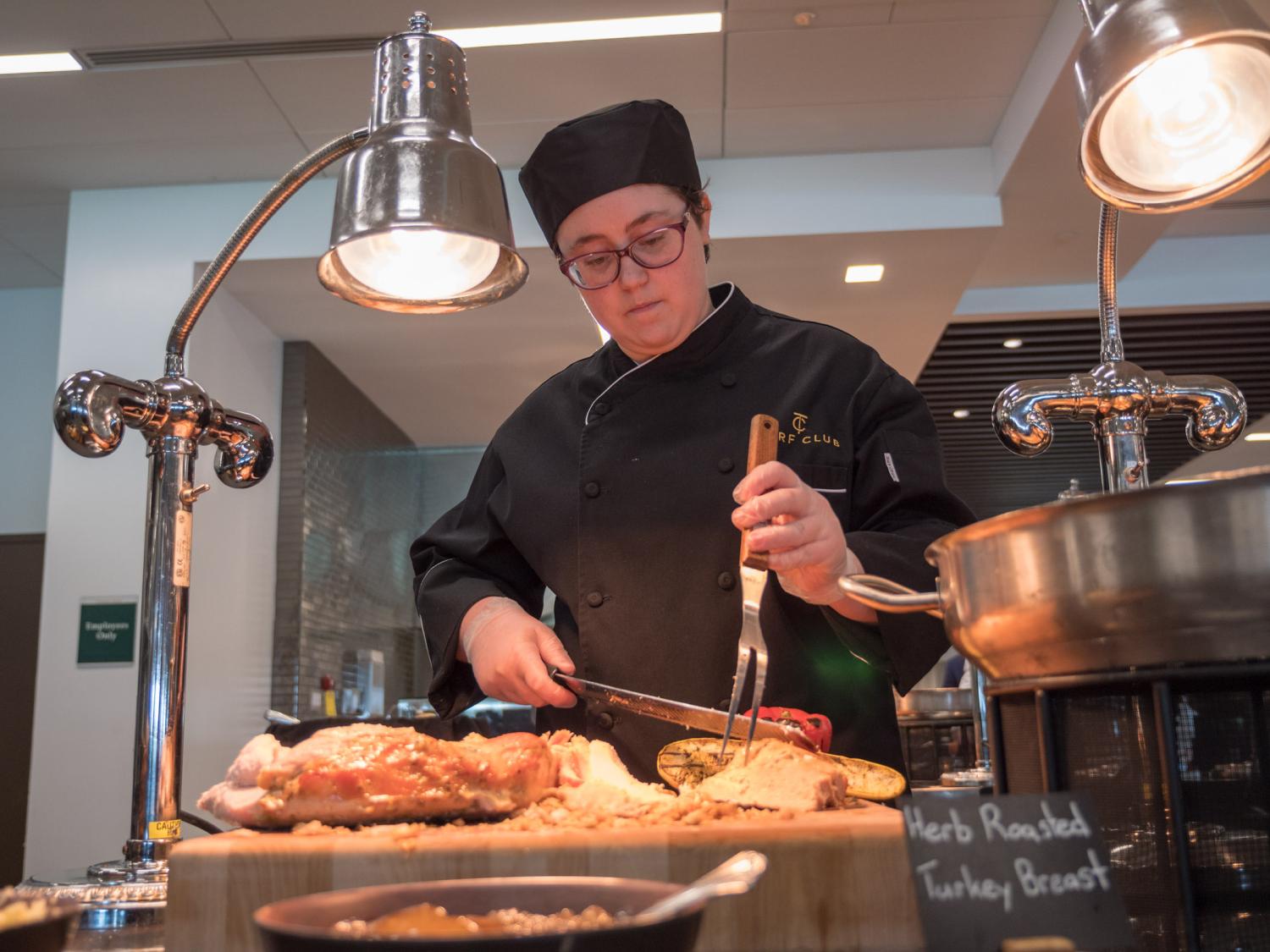 Penn College student Cynthia Setzer in a chef's coat and hat carving meat.