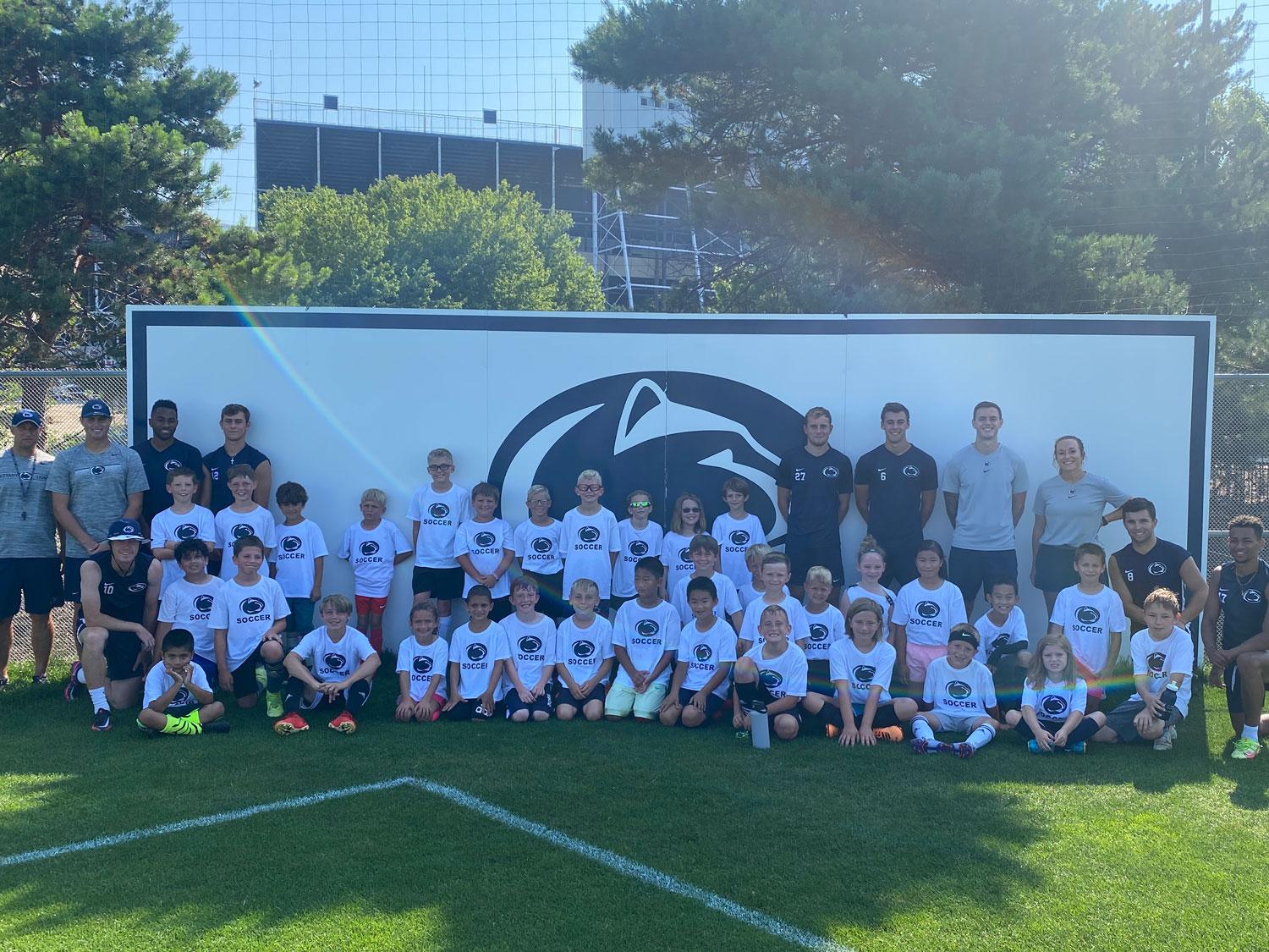 Penn State soccer players and coaches lined up in front of a Nittany Lion.