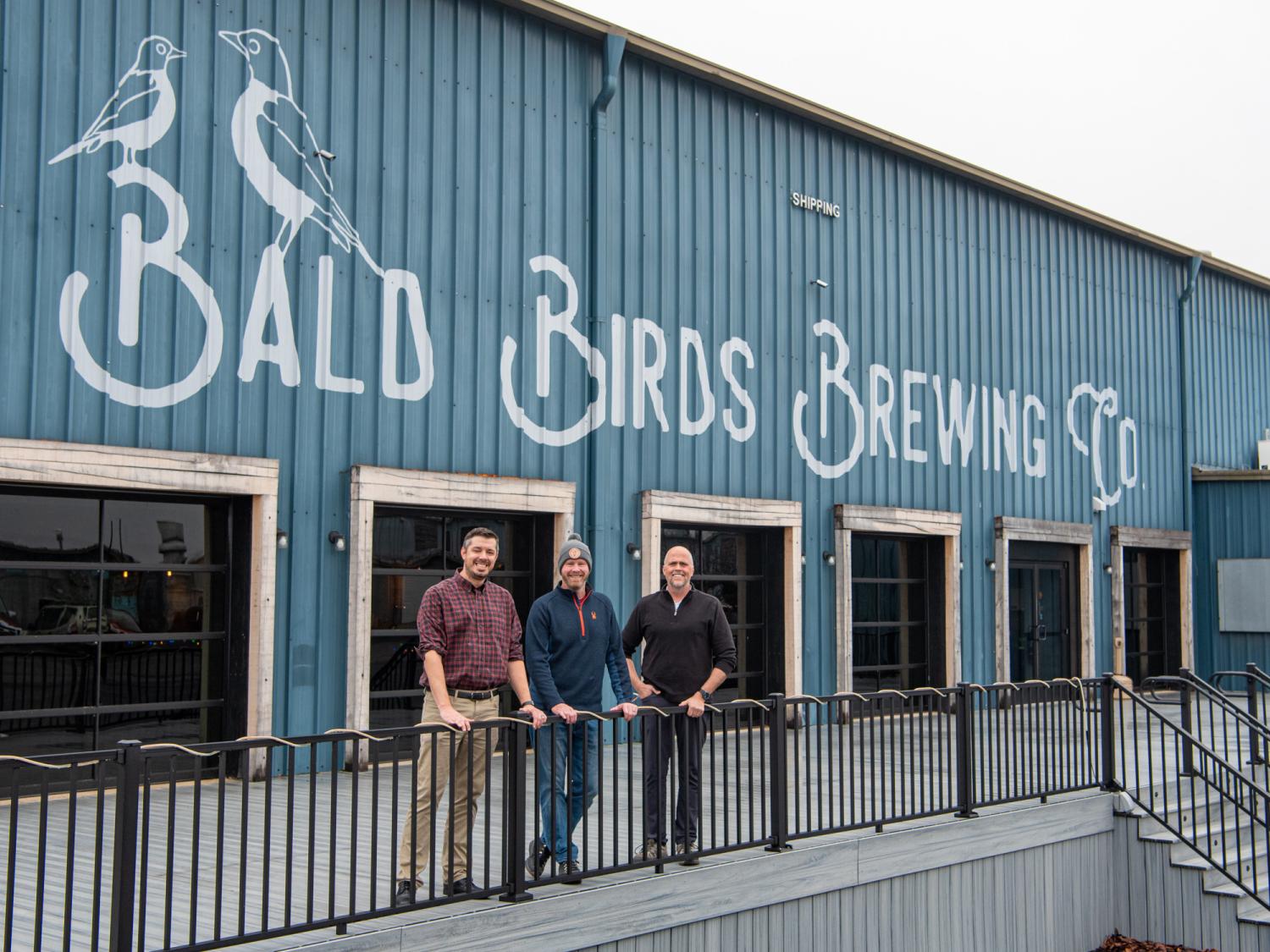 Three people stand in front of the Bald Birds Brewing Co sign
