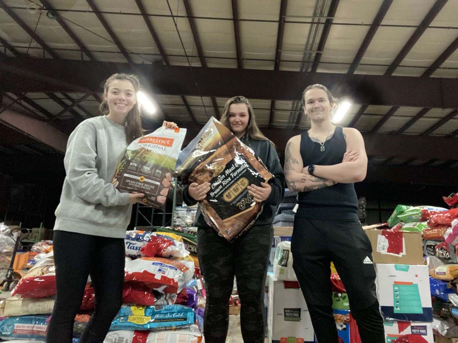 Three students standing in front of stacks of pet food in a warehouse.