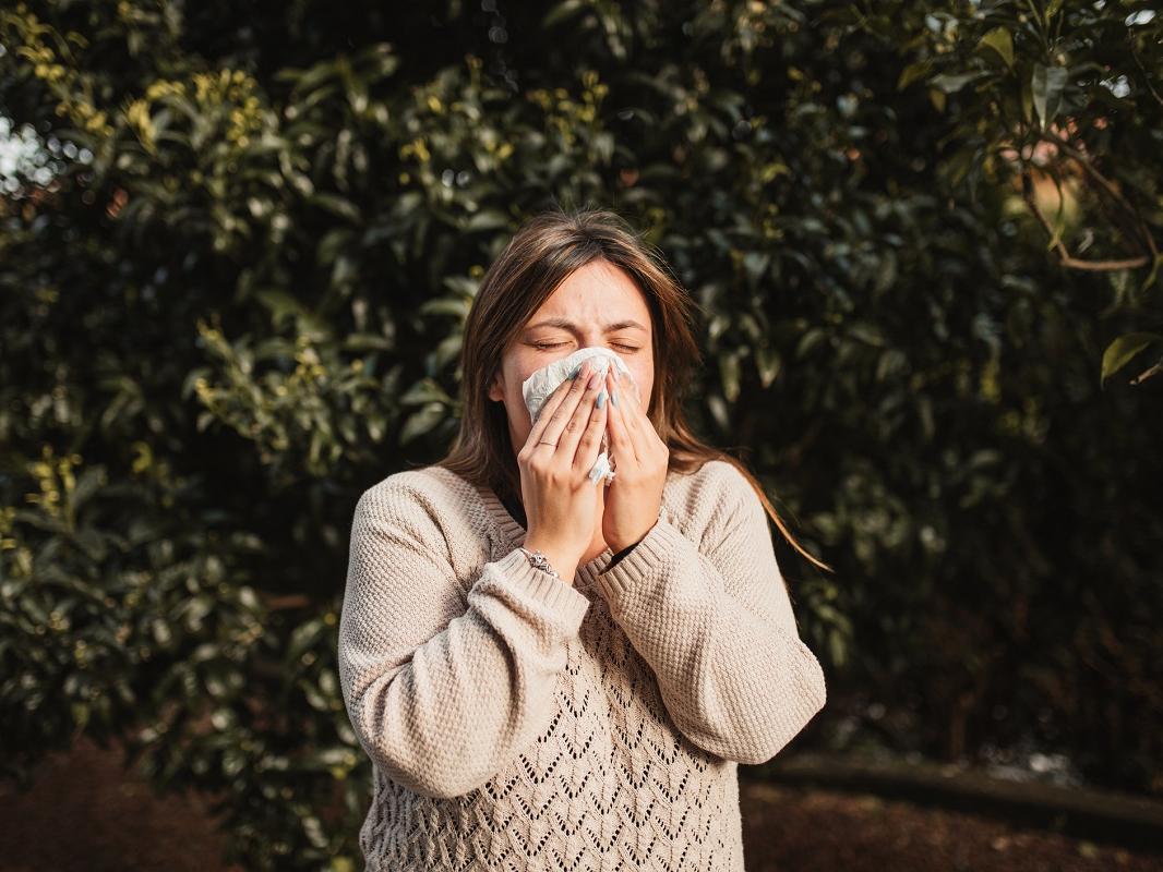 Young woman suffering spring allergy and blowing nose with a tissue.