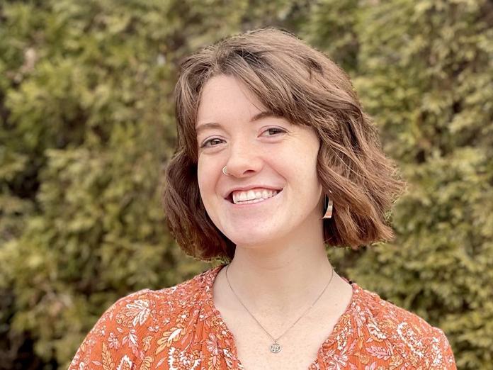 Head shot of a young woman with short brown hair posing in front of hedges