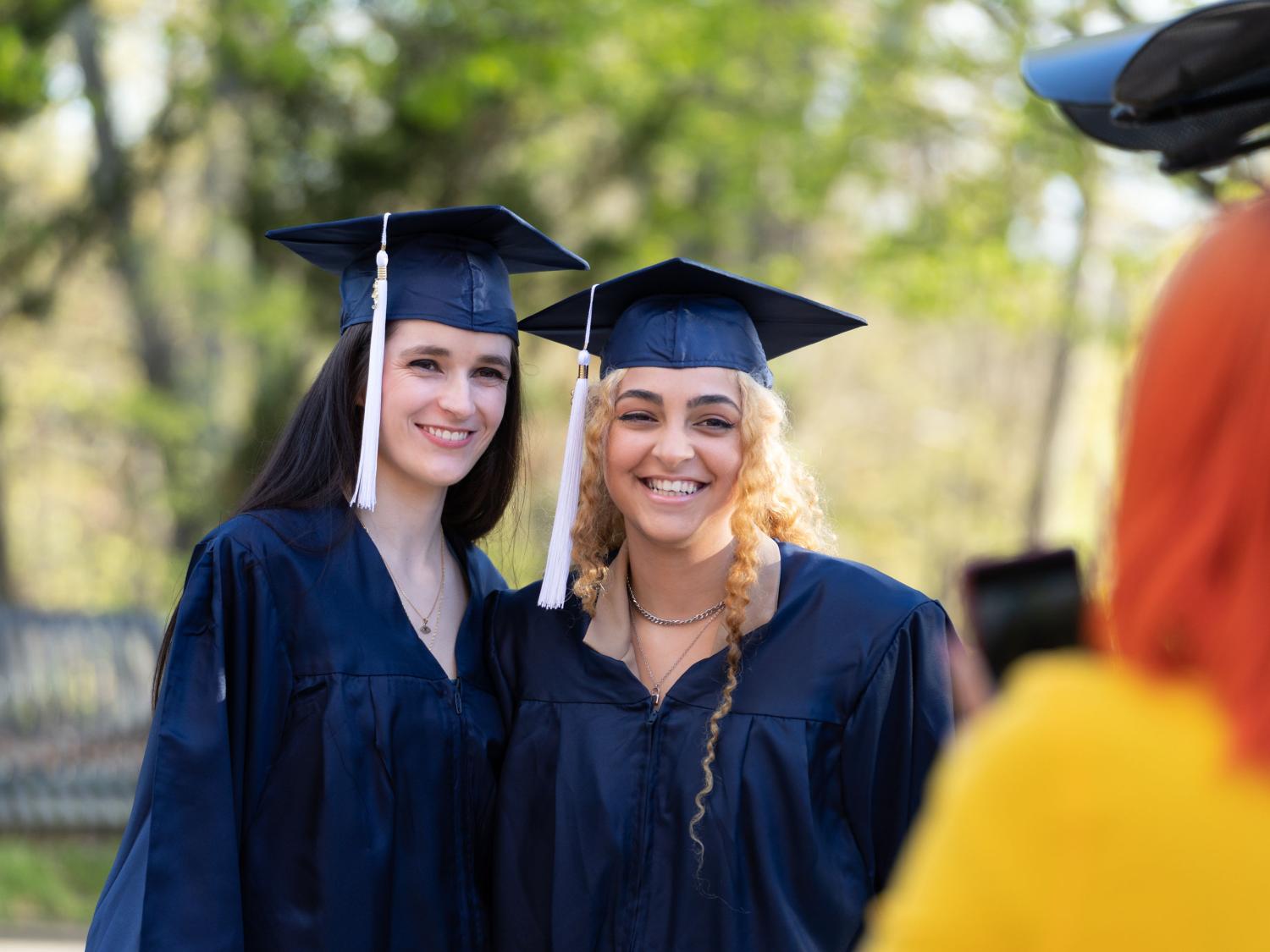 Female students in caps and graduation gowns smiling outdoors.