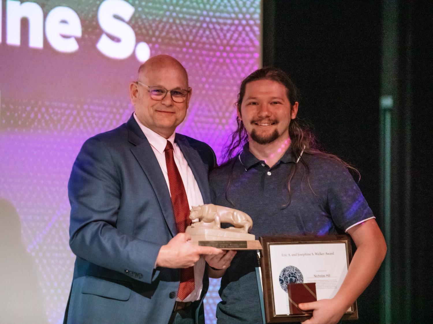 Two people stand holding a trophy