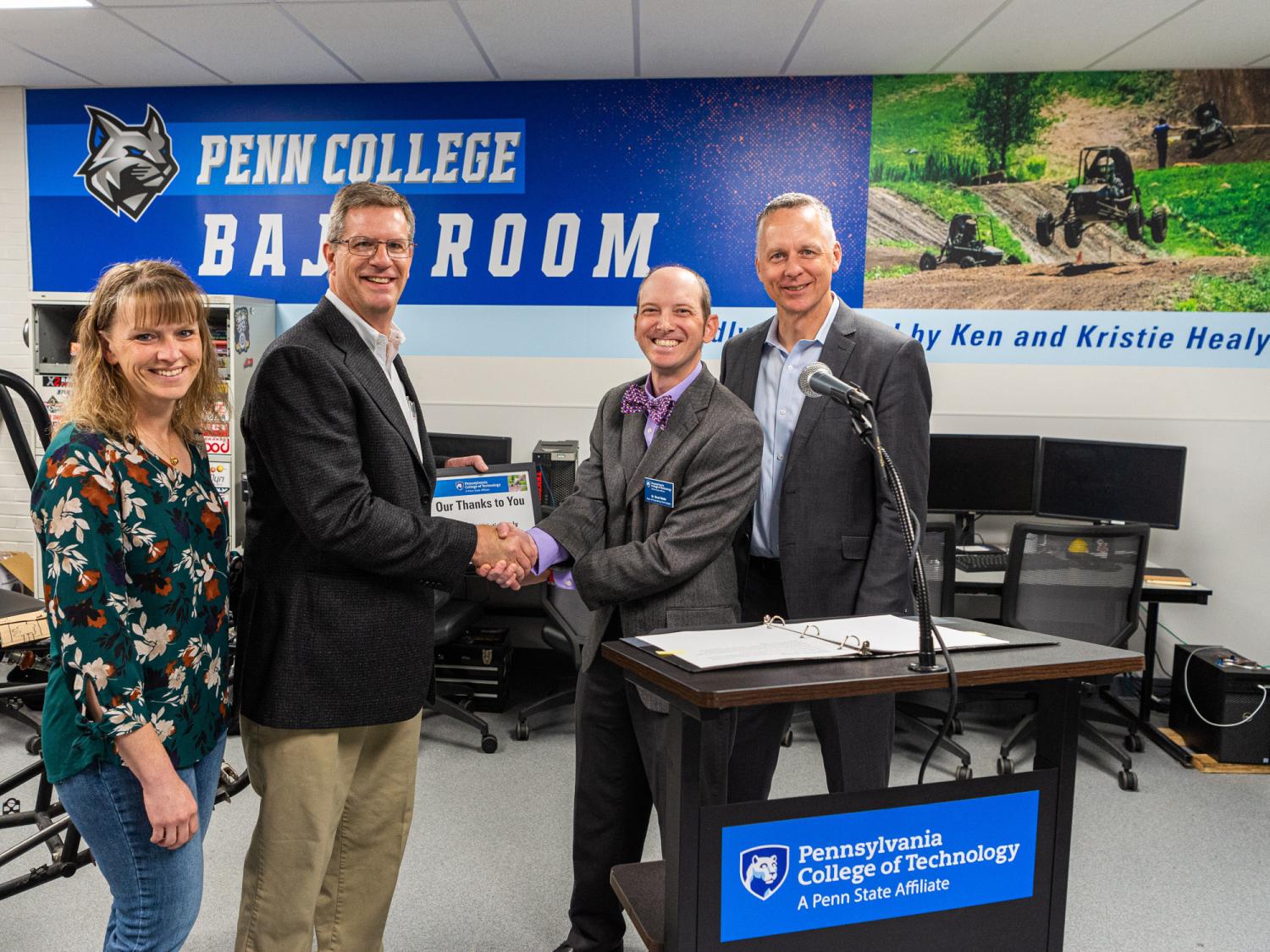 Four people stand in the new Baja Room at Penn College. Two of them are shaking hands.