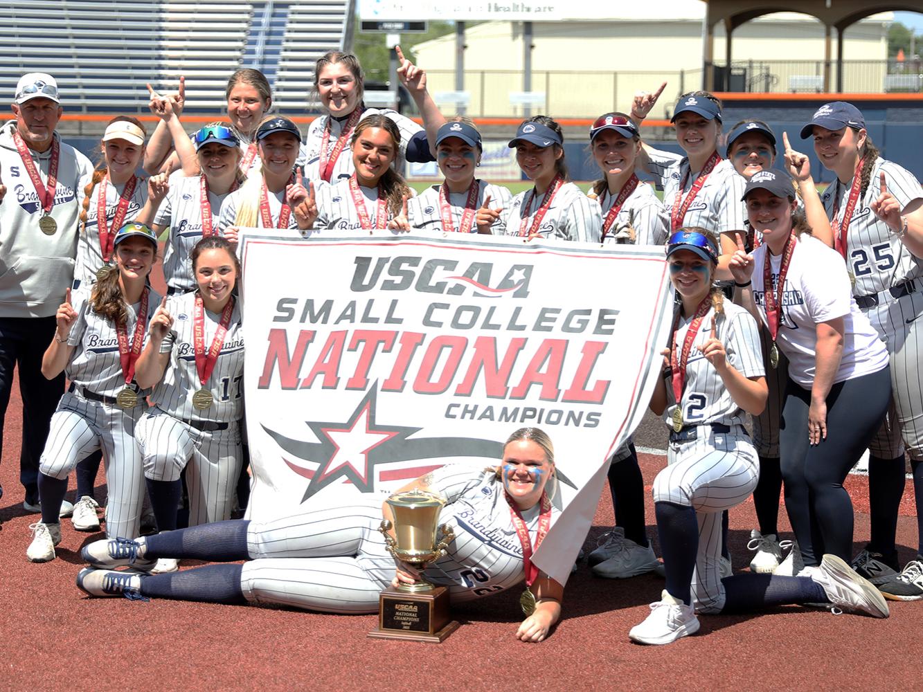 2023 Penn State Brandywine softball team posing with its championship banner and trophy