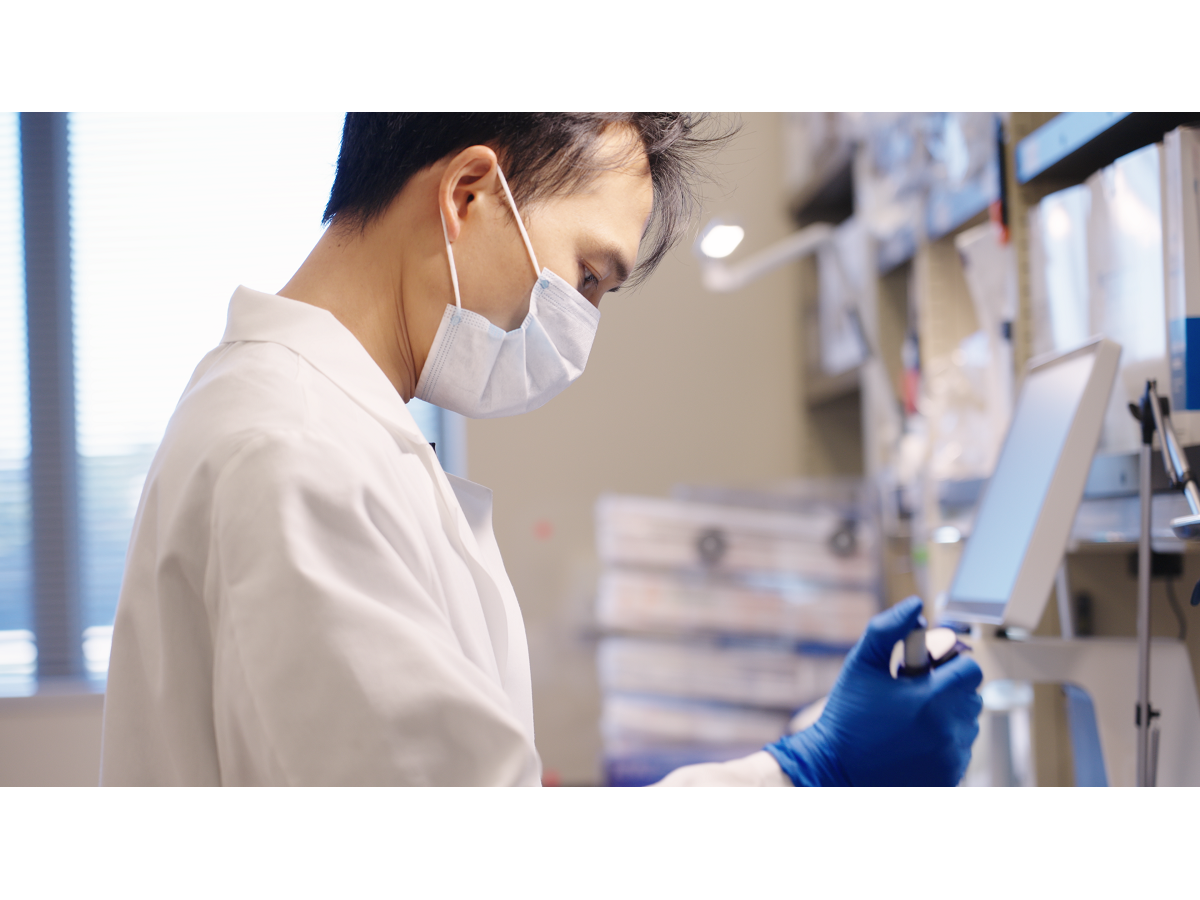 Jiaxing Chen, a bioinformatics and genomics doctoral student at Penn State College of Medicine and Penn State Huck Institutes of the Life Sciences, pipettes a solution in a laboratory while wearing gloves, a lab coat and a mask. 