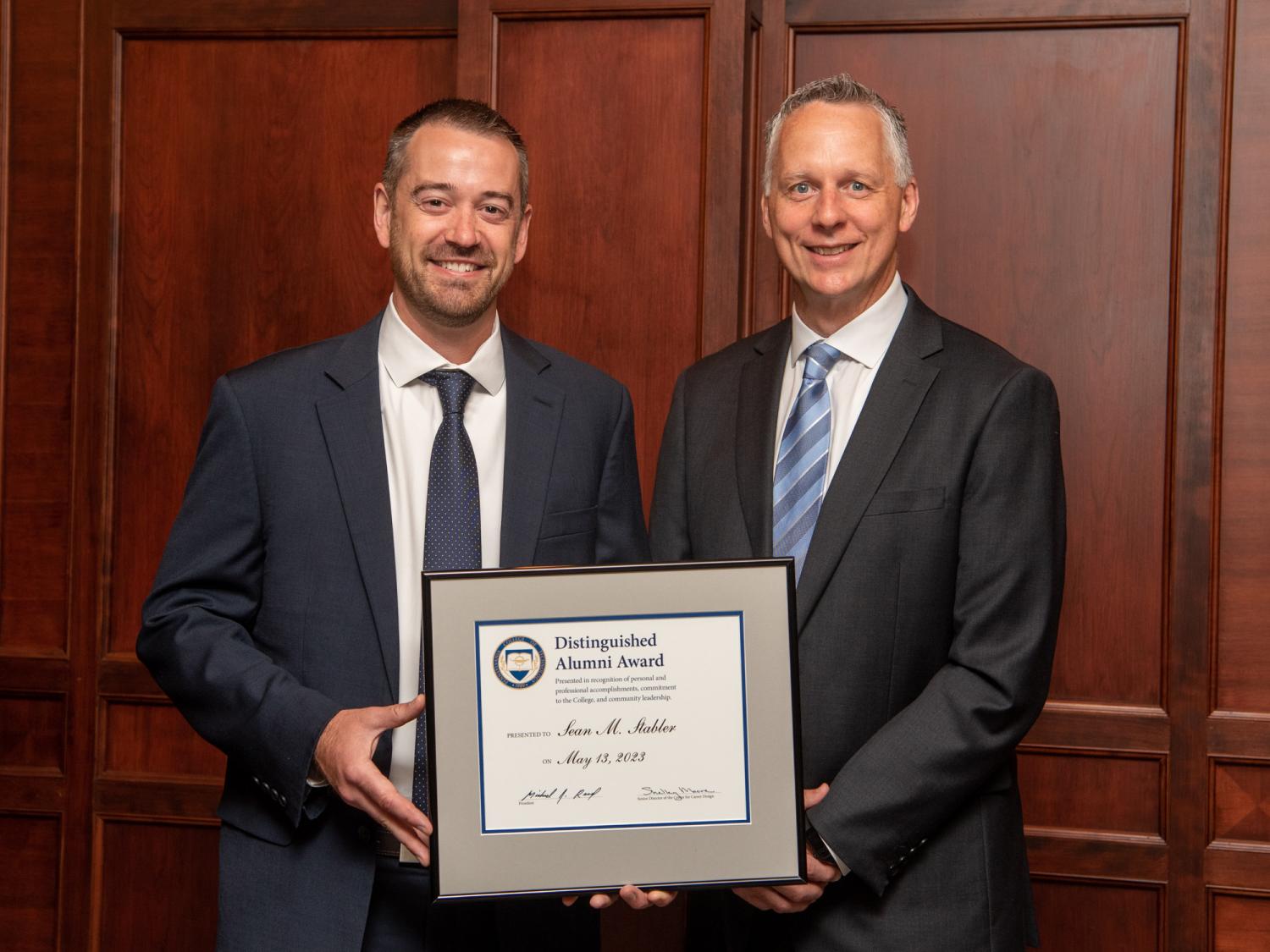 Two people standing together holding a framed award between them