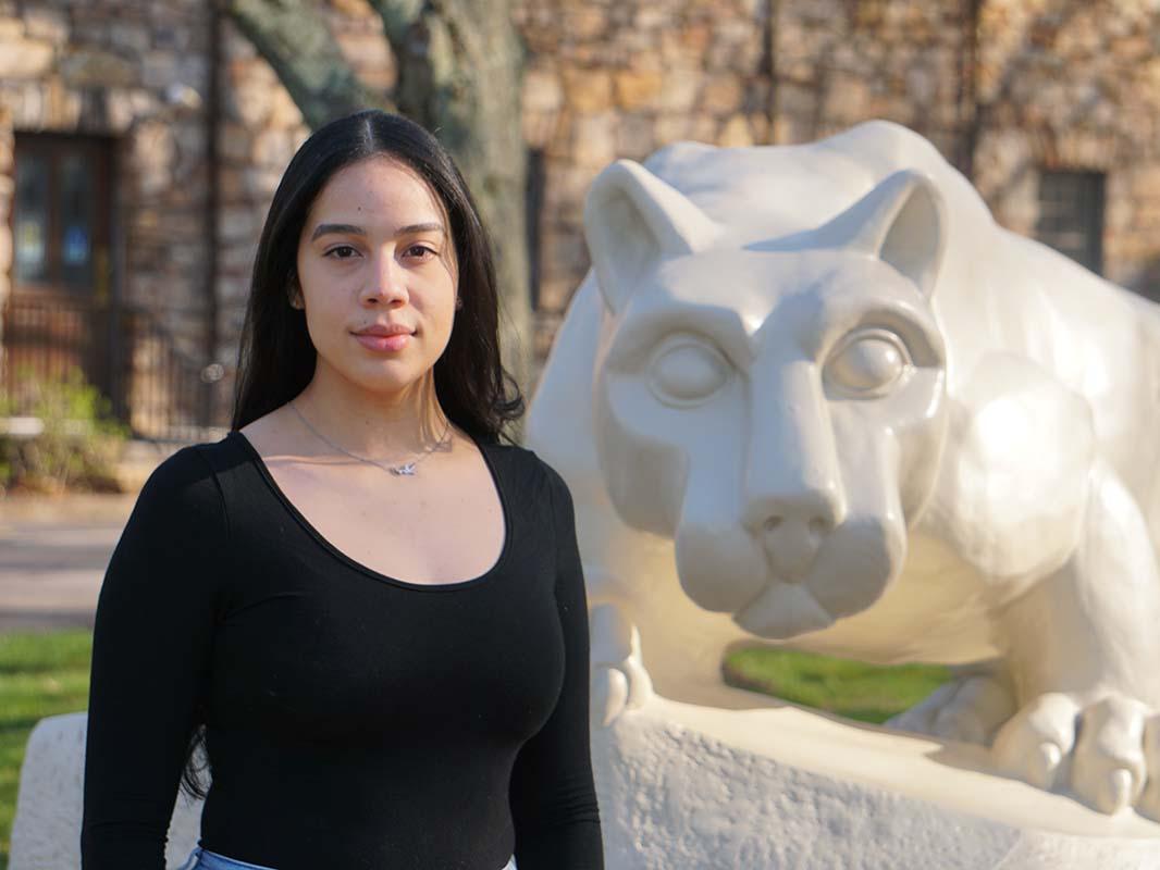 Woman with dark hair standing next to cream-colored Nittany Lion statue.