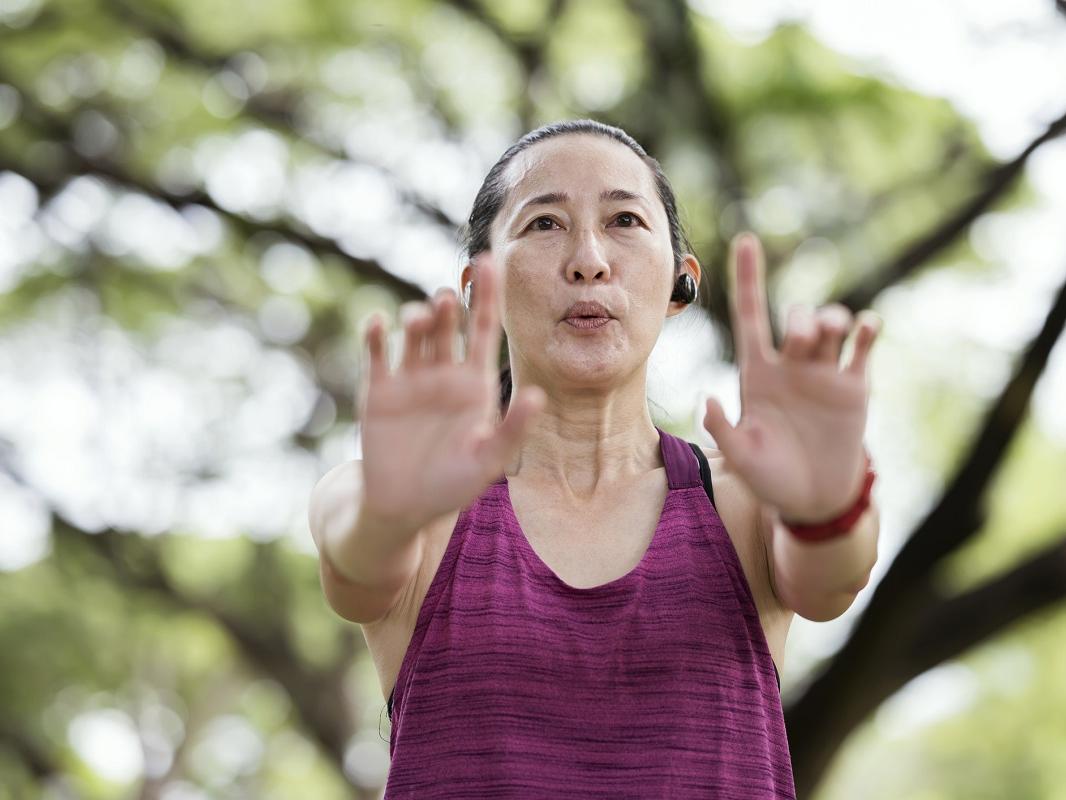 A woman practices qigong poses in a park.